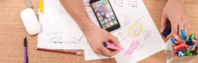 Man sitting at a table with various colored markers, highlighting sentences on a white paper. A messy desk with a monitor in front of him.