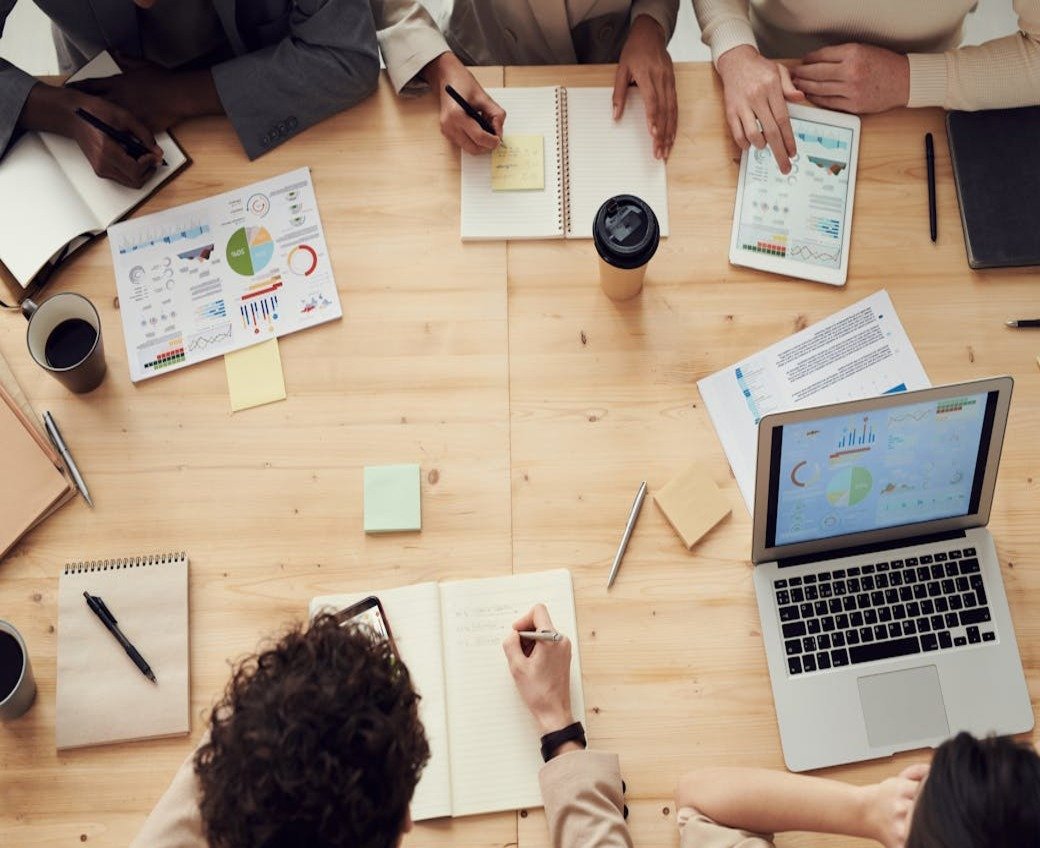 Employees at a digital agency sitting at a table during a meeting with laptops, reports, and notebooks.